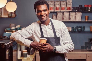 Afrika barista kahve ile iş günü süre üstünde belgili tanımlık sayaç kahve dükkanında eğilerek sonra rahatlatıcı kameraya gülümseyen.