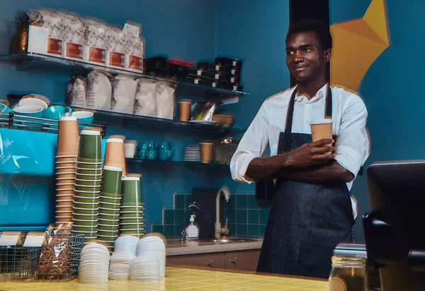 Portrait of a handsome African barista at counter of a trendy coffee shop.