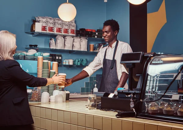 Barista afroamericano dando taza de café a su cliente femenino en la cafetería de moda . —  Fotos de Stock
