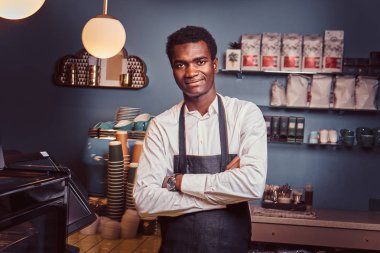 Sayaç trendy coffee shop çapraz kollu yakışıklı Afrika barista ayakta portresi.