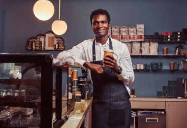 Afrika barista kahve ile iş günü süre üstünde belgili tanımlık sayaç kahve dükkanında eğilerek sonra rahatlatıcı kameraya gülümseyen.