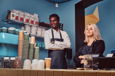 İki genç çok ırklı baristas welcomingly onların trendy kahve dükkanında ayakta önlük içinde.