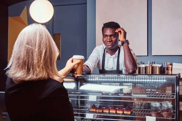 Αφρικανική αμερικανική barista δίνοντας φλιτζάνι καφέ του θηλυκό πελάτη στο μοντέρνο καφέ. — Φωτογραφία Αρχείου