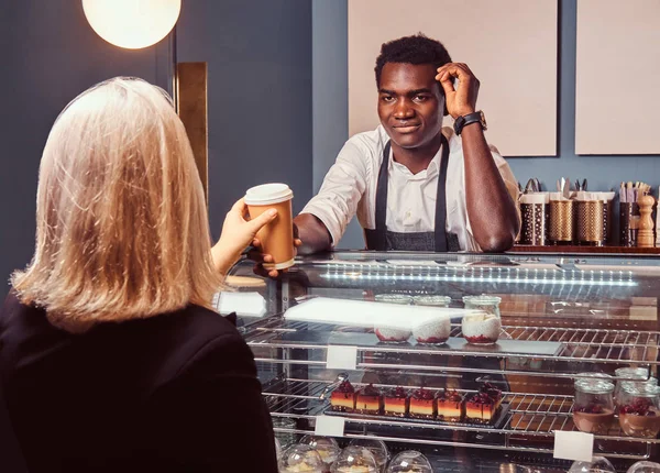 Barista afroamericano dando taza de café a su cliente femenino en la cafetería de moda . —  Fotos de Stock