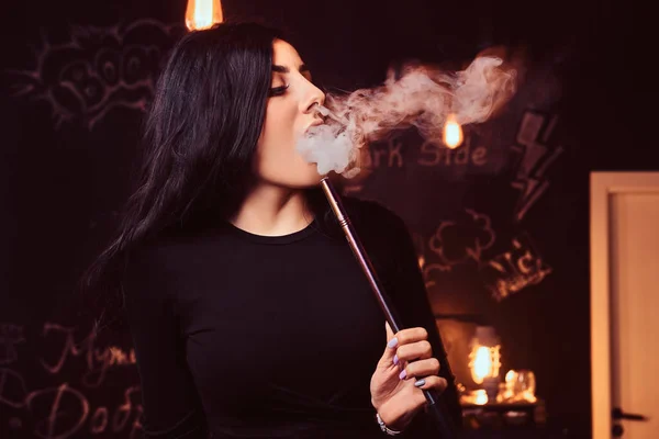 Nahaufnahme eines verführerischen brünetten Mädchens in schwarzem Top, das in einem Nachtclub oder einer Shisha-Bar eine Wasserpfeife raucht. — Stockfoto