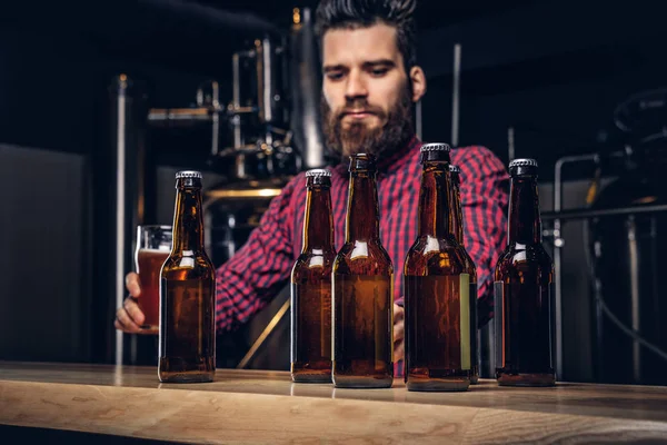 Foto met ambachtelijke bierflessen op de voorgrond en gebaarde mannelijke drinken op de achtergrond. — Stockfoto