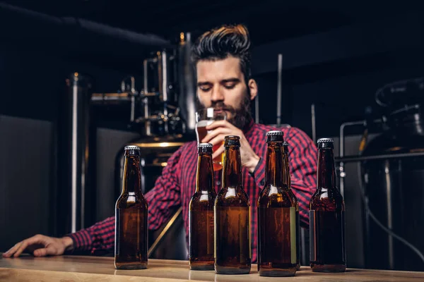 Foto met ambachtelijke bierflessen op de voorgrond en gebaarde mannelijke drinken op de achtergrond. — Stockfoto