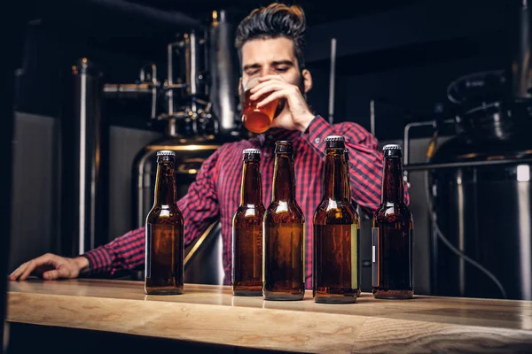 Foto met ambachtelijke bierflessen op de voorgrond en gebaarde mannelijke drinken op de achtergrond. — Stockfoto