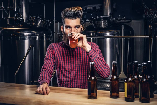 Hipster man met stijlvolle baard en haren drinken bier aan de bar zitten teller in indie brouwerij. — Stockfoto