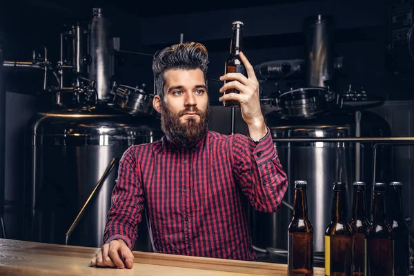 Hipster macho con barba elegante y el pelo bebiendo cerveza sentado en el mostrador del bar en la fábrica de cerveza indie . —  Fotos de Stock