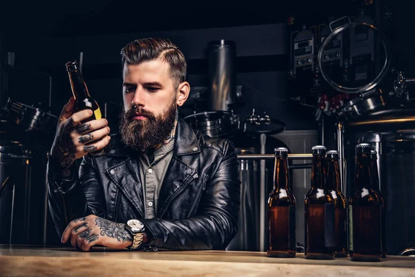 Elegante motorista barbudo vestido chaqueta de cuero negro sentado en el mostrador del bar en la fábrica de cerveza indie . — Foto de Stock