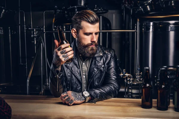Стильный бородатый байкер в черной кожаной куртке сидит за барной стойкой в инди-пивоварне . — стоковое фото