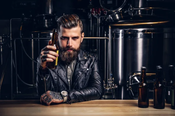 Elegante motorista barbudo vestido chaqueta de cuero negro sentado en el mostrador del bar en la fábrica de cerveza indie . — Foto de Stock