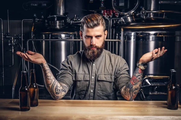 Portrait of a confident tattooed hipster male with stylish beard and hair in shirt in the indie brewery. — Stock Photo, Image