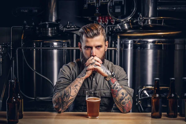 Retrato de un hombre hipster tatuado pensativo con barba elegante y pelo en la camisa en la fábrica de cerveza indie . — Foto de Stock