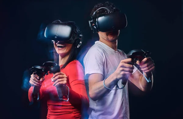 Happy friends playing video games wearing virtual reality glasses with controllers. Isolated on dark background.