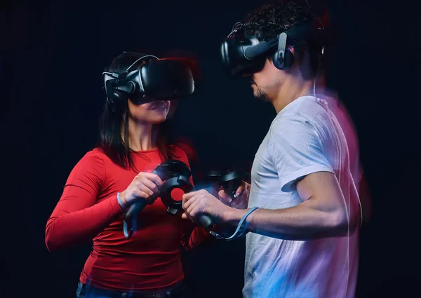 Young couple playing video games wearing virtual reality glasses with controllers.