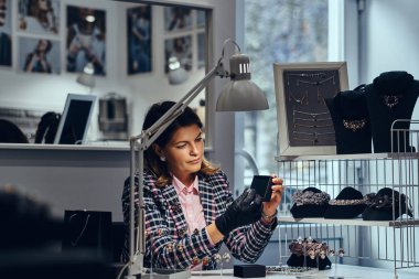 Kadın takı işçi zarif iş masada oturan giymiş ve muayene takı yapmak.