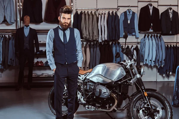 穿着优雅的男子摆在口袋附近的复古运动摩托车在男装服装店. — 图库照片