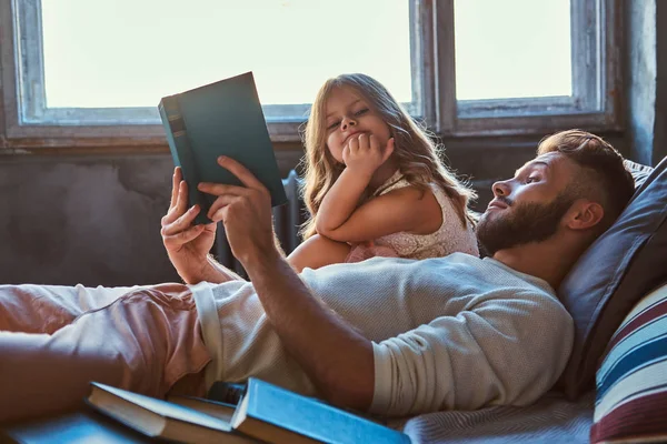 Bonito jovem pai lendo livro de histórias sua filhinha na cama . — Fotografia de Stock