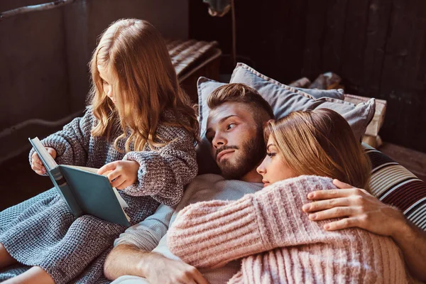 Mãe, pai e filha lendo o livro de histórias juntos enquanto estavam deitados na cama . — Fotografia de Stock