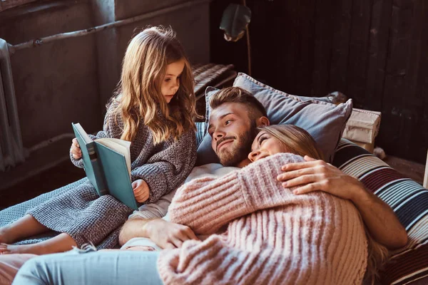 Mom, dad and daughter reading storybook together while lying on bed. — Stock Photo, Image