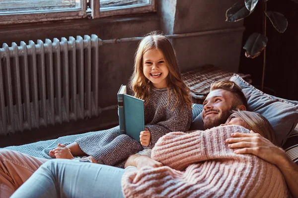 Mãe, pai e filha lendo o livro de histórias juntos enquanto estavam deitados na cama . — Fotografia de Stock