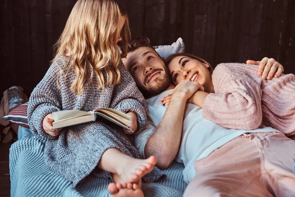 Mamma, papà e figlia leggono insieme il libro di fiabe mentre sono sdraiati sul letto . — Foto Stock