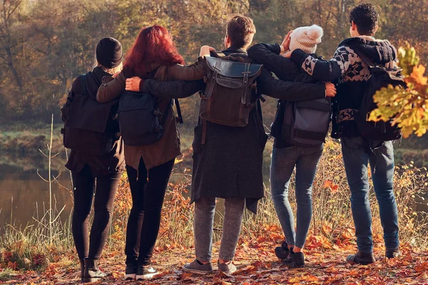 Widok z tyłu młodych przyjaciół razem przytulanie i patrząc na jeziorze w piękny jesienny Las. — Zdjęcie stockowe