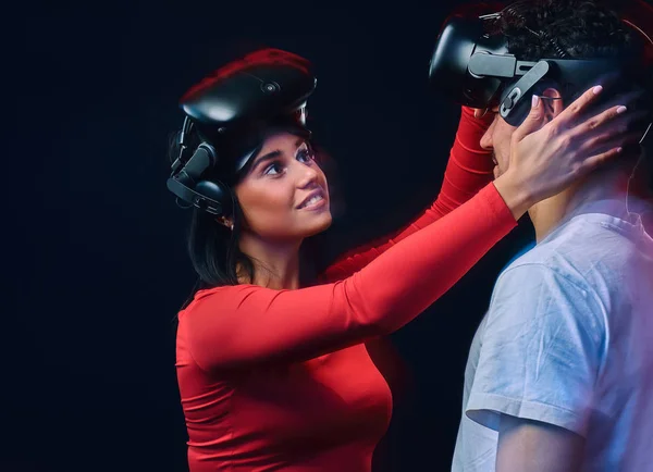 Joven chica alegre ajusta gafas de realidad virtual en su novio. Pareja de jugadores con auriculares VR . — Foto de Stock