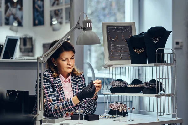 Trabajadora de joyas elegantemente vestida sentada en la mesa de trabajo y hacer el examen de la joyería . —  Fotos de Stock