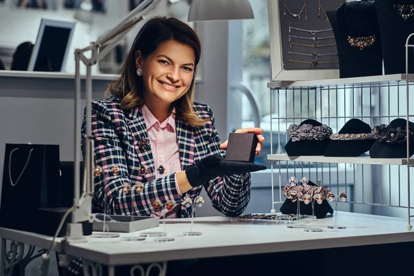 Female jewelry worker showing a black box with for precious earrings in a luxury jewelry store.