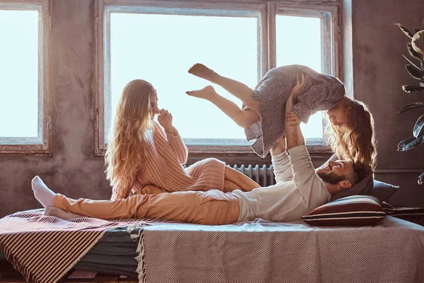 Mãe, pai e filha na cama. Pai brincando com filha adorável no quarto . — Fotografia de Stock