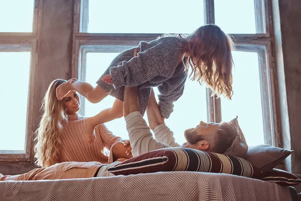 Mom, dad and daughter in bed. Father playing with adorable daughter in bedroom.