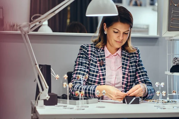 Vrouw verkoper pakt kostbare oorbellen in een vak voor haar cliënt in een luxe sieraden winkel. — Stockfoto