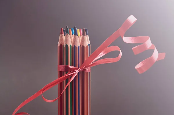 Sekelompok pensil berwarna-warni dihiasi dengan pita hadiah merah . — Stok Foto