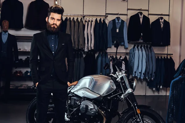 胡子时尚男子身着黑色西装摆在口袋附近复古运动摩托车在男装店. — 图库照片