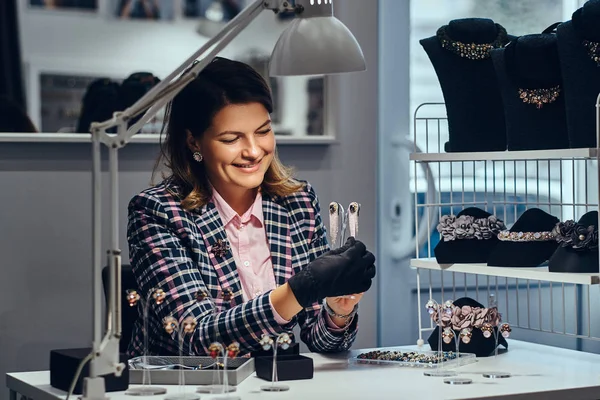 Trabalhadora de jóias feminina mostrando belos brincos preciosos com pedras preciosas em uma joalharia de luxo . — Fotografia de Stock