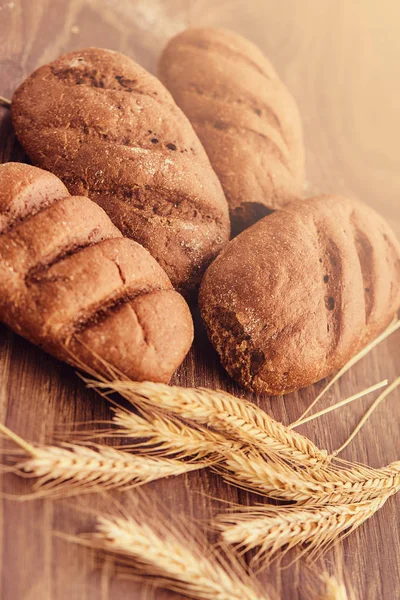 Вкусные свежие хлебобулочные изделия и колоски пшеницы на деревянном фоне . — стоковое фото