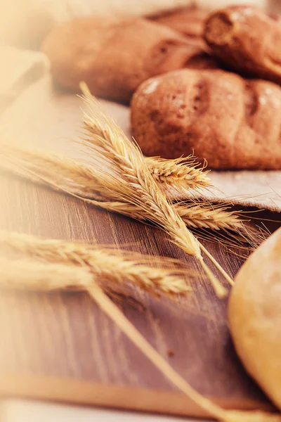 Delicious freshly bakery products and spikelets of wheat on wooden background. — Stock Photo, Image
