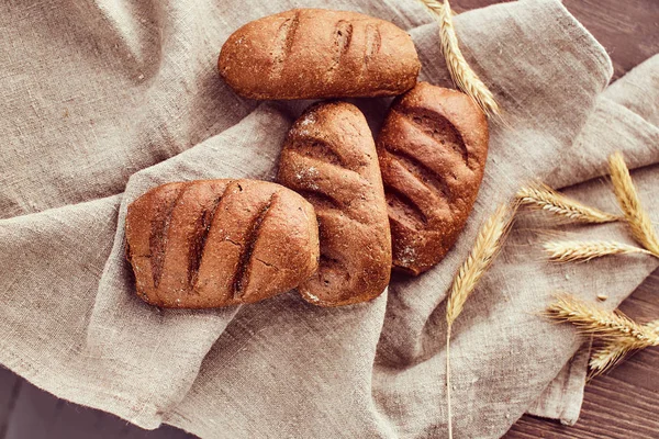Freshly baked buns and spikelets of wheat lying on a linen cloth. — Stock Photo, Image