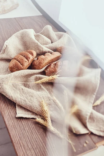 Panini appena sfornati e spighe di grano adagiate su un panno di lino . — Foto Stock