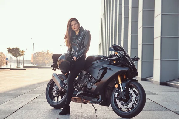 Una hermosa motociclista apoyada en su supermoto fuera de un edificio en un día soleado . —  Fotos de Stock