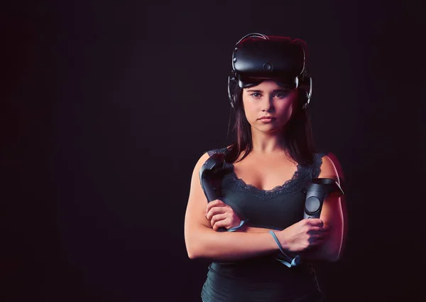 一个年轻女子的肖像戴着虚拟现实眼镜和握操纵杆, 摆在交叉的胳膊, 看着相机. — 图库照片