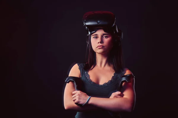 Retrato de uma jovem mulher vestindo óculos de realidade virtual e segura joysticks, posando com os braços cruzados, olhando para a câmera . — Fotografia de Stock