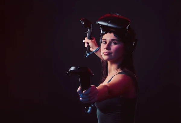 Красива молода жінка в гарнітурі віртуальної реальності і тримає джойстики, позує на камеру . — стокове фото