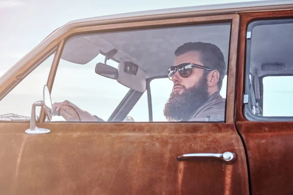 Barbudo macho vestido com jaqueta de couro marrom dirigindo um carro retro . — Fotografia de Stock