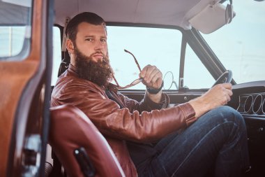 Dalgın şık erkek güneş gözlüğü eski moda kıyafetler giymiş açık kapı ile ayarlanmış bir retro arabanın direksiyonuna oturur tutar.