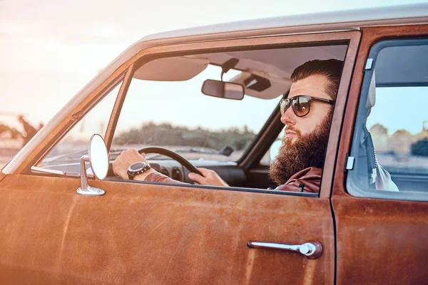 Vousatý muž v sluneční brýle na sobě koženou bundu retro autem. — Stock fotografie