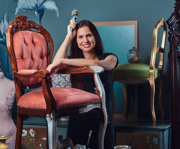 Donna artista felice tiene pennello e appoggiato su una sedia vintage in laboratorio . — Foto Stock